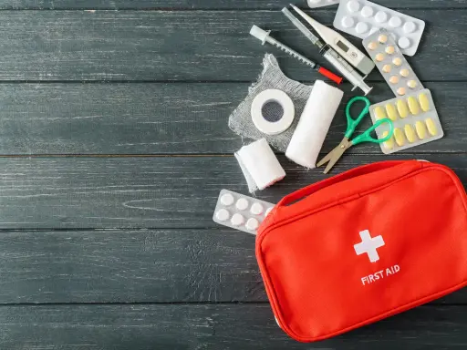 Czerwona apteczka z wyposażeniem: plastry, bandaże, nożyczki, termometr, strzykawki i tabletki. Czy trzeba mieć apteczkę w aucie? Tak, dla bezpieczeństwa!