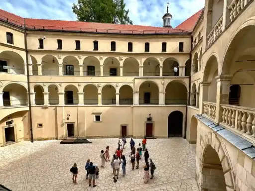 Dziedziniec zamku w Ojcowie z arkadowymi krużgankami i grupą turystów.