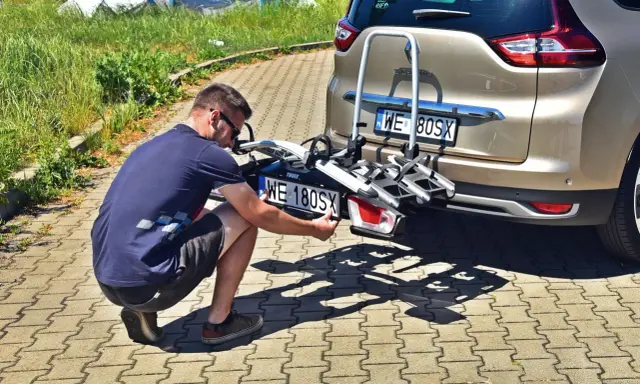 Mężczyzna montuje trzecią tablicę rejestracyjną WE 180SX na bagażniku rowerowym przy samochodzie.
