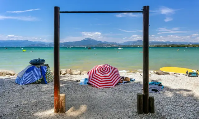 Słoneczne plaże nad jeziorem Garda, z parasolami, leżakami i wodnymi atrakcjami w tle.
