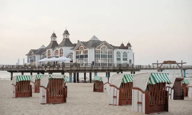 Plaża na wyspie Rugia z charakterystycznymi koszami plażowymi i molo prowadzącym do białego pawilonu.