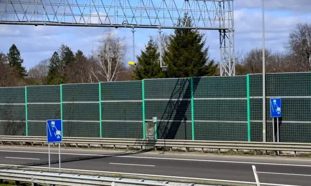 Znak informujący o odcinkowym pomiarze prędkości S3. Za ekranami akustycznymi widać drzewa i niebo.
