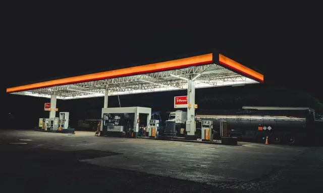 Nocna stacja paliw w Polsce, oświetlona neonami, z dystrybutorami i cysterną.