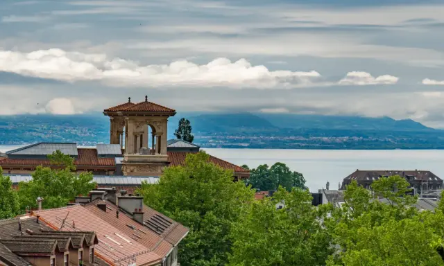 Widok na szwajcarskie miasto nad jeziorem Genewskim, z charakterystyczną wieżą i dachami budynków.