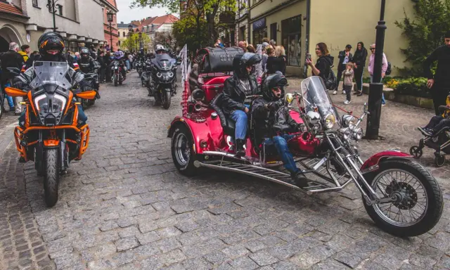 Parada motocykli i trójkołowców na brukowanej ulicy. W tle widzimy ludzi i budynki. To może być początek podróży szwecja motocyklem.