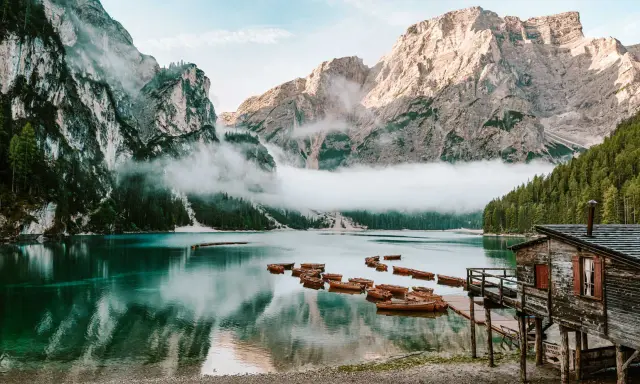 Spokojne jezioro w Dolomitach, Tyrol Włochy, z łodziami przy drewnianym molo i mgłą otulającą góry.