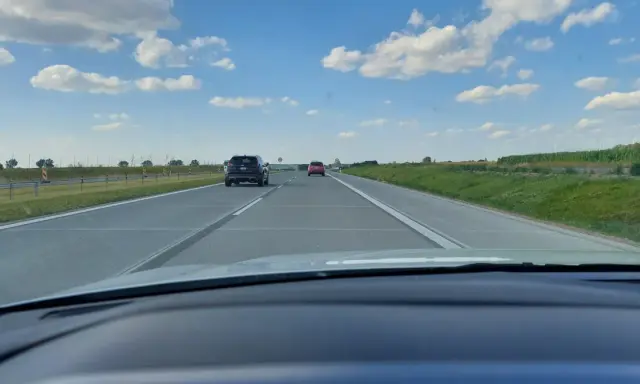 Jadąc na S7, widzimy pola i chmury. Samochody poruszają się po pustej drodze.