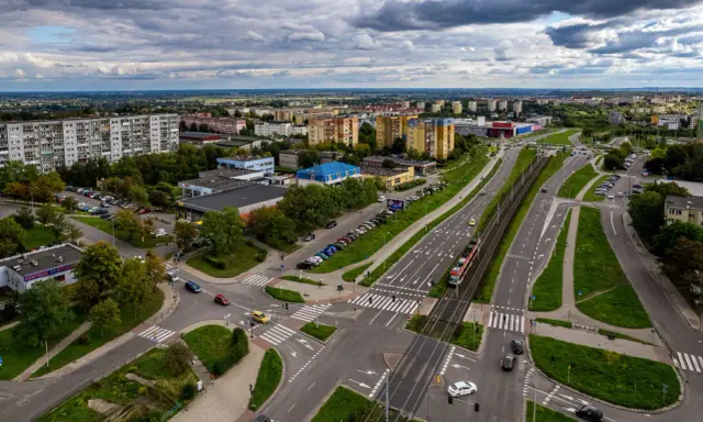 Widok z lotu ptaka na ruchliwe skrzyżowanie w Gdańsku Chełmie, z tramwajem, samochodami i budynkami mieszkalnymi w tle.