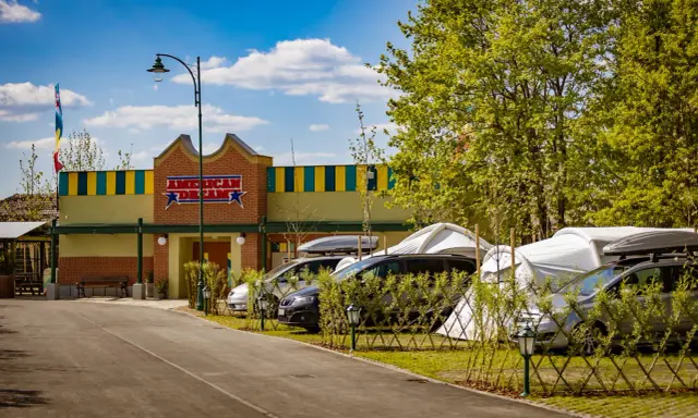 Zator Energylandia trasa: parking z samochodami i namiotami pod budynkiem "American Dream" w słoneczny dzień.