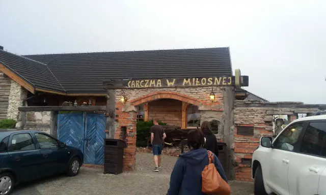 Karczma w Miłośnej, jedna z restauracji na trasie, zaprasza gości. Widać samochody i ludzi wchodzących do środka.