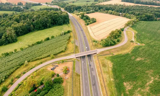 Nowa sól trasa przecina zielone pola i lasy, łącząc odległe zakątki. Widok z lotu ptaka ukazuje drogę, most i samochody w ruchu.