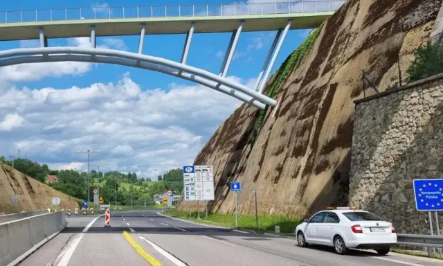 Biały samochód na granicy Polski, przygotowuje się do podróży do Danii samochodem. Nad drogą wznosi się imponujący most.