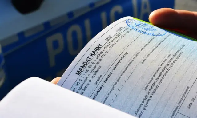 Dłoń trzyma mandat karny. Czy można uniknąć płacenia mandatu? Dokument zawiera rubryki do wypełnienia, np. odmowa przyjęcia.