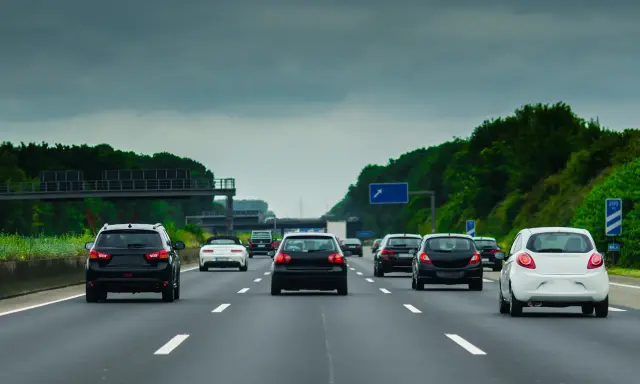 Ruch samochodów na niemieckiej autostradzie A8 pod pochmurnym niebem. Widać kilka czarnych i jeden biały samochód jadący pasem.