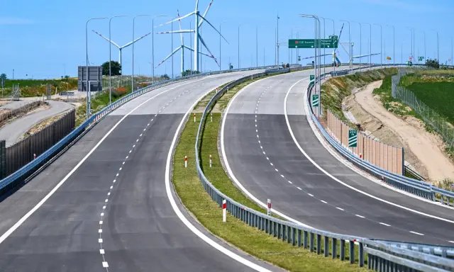 Nowa droga S6 z wiatrakami w tle. Pusta autostrada z zielonym pasem zieleni i barierami.