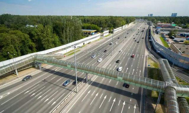 Szerokie drogi w Rosji z zielonym, przeszklonym mostem dla pieszych. Ruch samochodowy na wielopasmowej autostradzie.