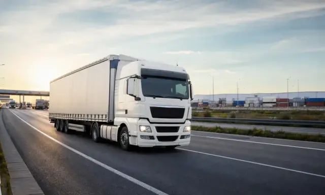 Biała ciężarówka jedzie autostradą w Holandii. W tle widać magazyny i kontenery.
