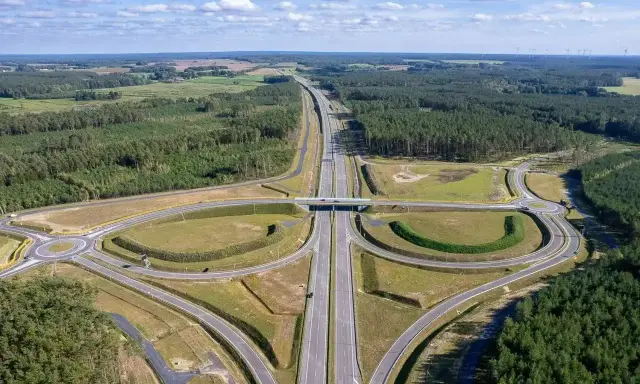 Węzeł drogowy na trasie Poznań-Kołobrzeg. Nowoczesna infrastruktura drogowa otoczona lasami i polami.