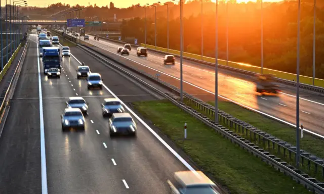 Zachód słońca nad Via Baltica. Samochody i ciężarówki pędzą autostradą w złotym blasku.