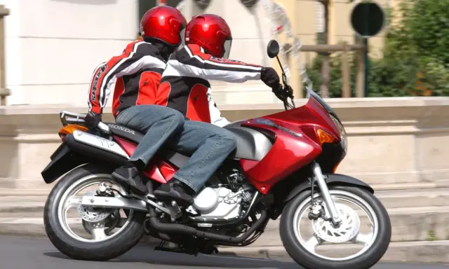 Dwie osoby w kaskach i kurtkach jadą na czerwonym motocyklu. Idealny na pierwsze prawo jazdy na 125.