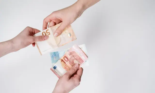 Dwie ręce przekazują sobie banknoty euro. W Austrii obowiązuje euro, co widać na przykładzie tych banknotów.