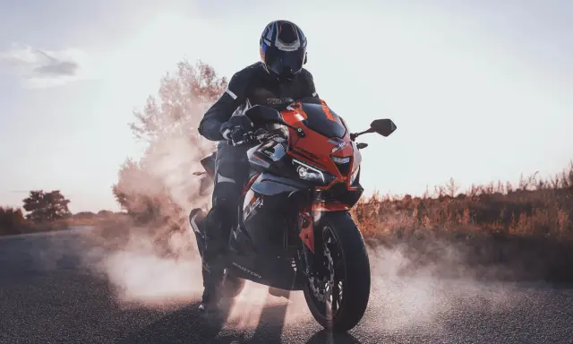 Motocyklista w kasku i kombinezonie na sportowym motocyklu, otoczony dymem. Czy motorem można jeździć po autostradzie? Tak, jeśli spełnia określone wymogi.