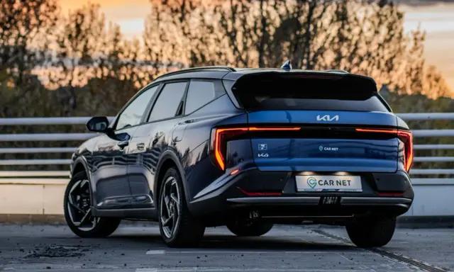 Niebieskie Kia EV6 gotowe na podróż z Poznania do Jeleniej Góry. Zachód słońca nad drzewami.