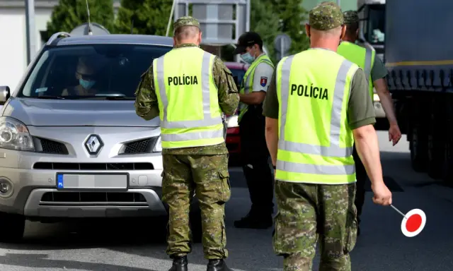 Policjanci w kamizelkach odblaskowych kierują ruchem podczas przejazdu przez Słowację. Kierowca w masce zatrzymuje się do kontroli.