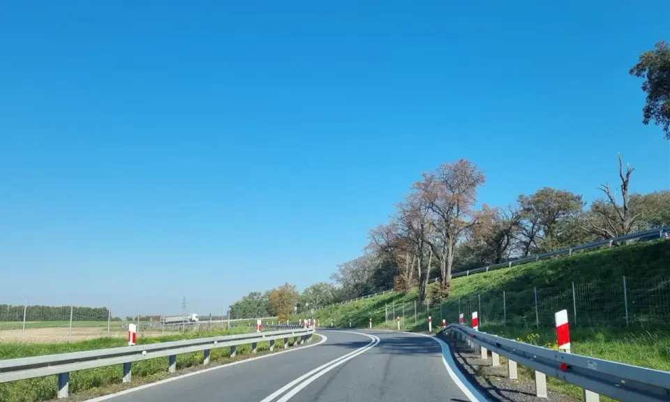 Słupki na autostradzie wyznaczają zakręt drogi. Jasne niebo i zielone pobocze tworzą malowniczy krajobraz.