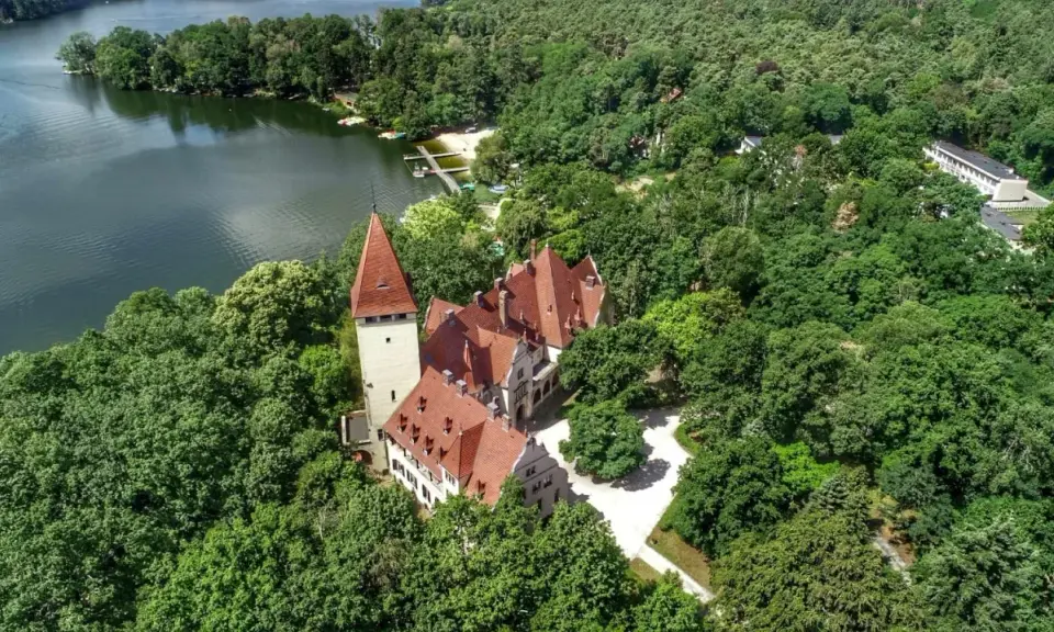 Zamek w Lubniewicach, otoczony bujną zielenią, malowniczo położony nad jeziorem.