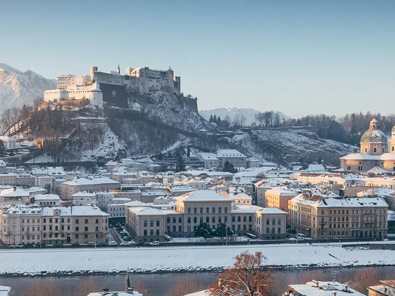 Salzburg zimą. Majestatyczna twierdza Hohensalzburg góruje nad zasypanym śniegiem miastem i rzeką Salzach.