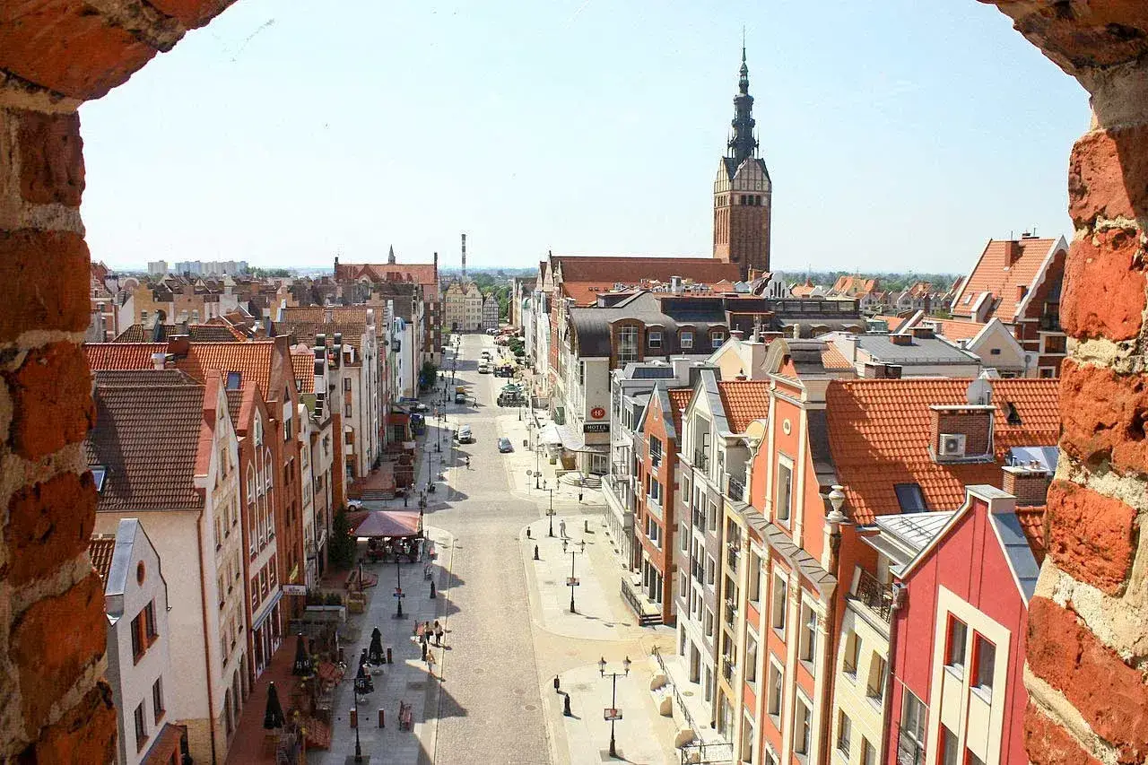 Widok na ulicę w **starym mieście Elbląg** z ceglanego muru. W oddali widać wieżę kościoła.