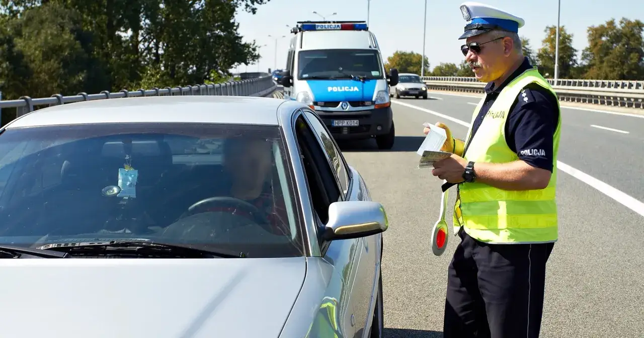 Policjant wypisuje mandat za przekroczenie prędkości o 20 km/h. Kierowca zatrzymany na drodze.