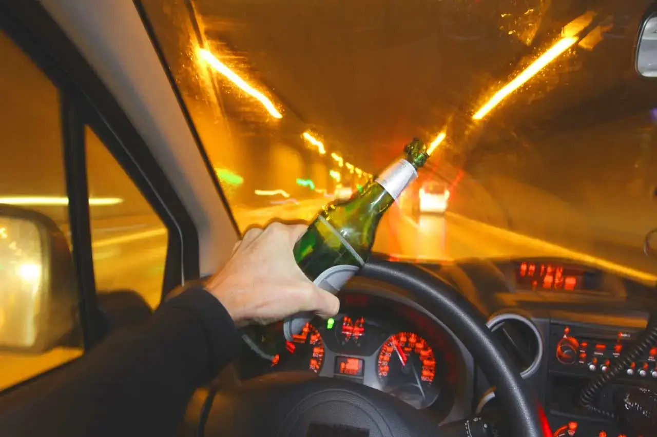 Ręka trzymająca butelkę piwa za kierownicą. Kierowca zastanawia się, czy 0 2 promila to już za dużo alkoholu.