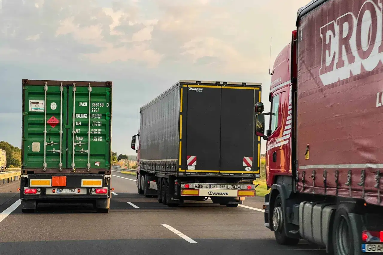 Trzy ciężar&oacute;wki na autostradzie. Jedna zielona z kontenerem, druga czarna i czerwona. Może to scena z filmu o mandacie za wyprzedzanie tirem.