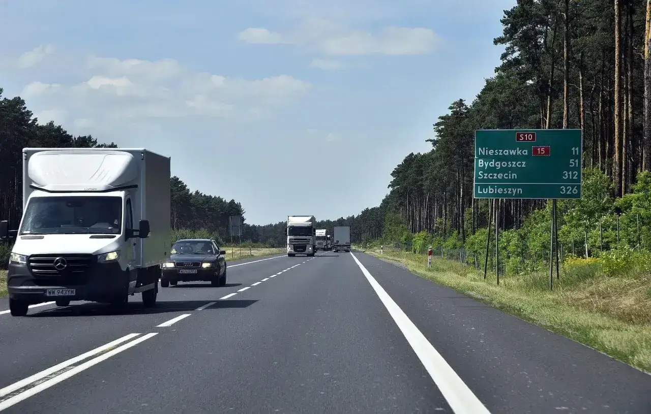 Droga jednojezdniowa wśród lasu. Na poboczu znak z kierunkami: Nieszawka, Bydgoszcz, Szczecin, Lubieszyn.