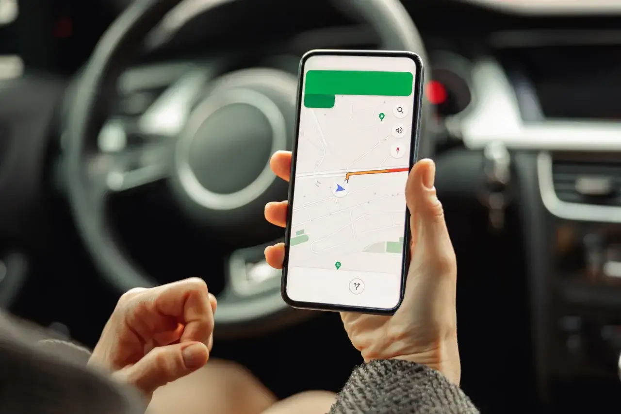 Kierowca trzyma smartfon z nawigacją, zastanawiając się, ile punktów karnych za telefon grozi za takie zachowanie.