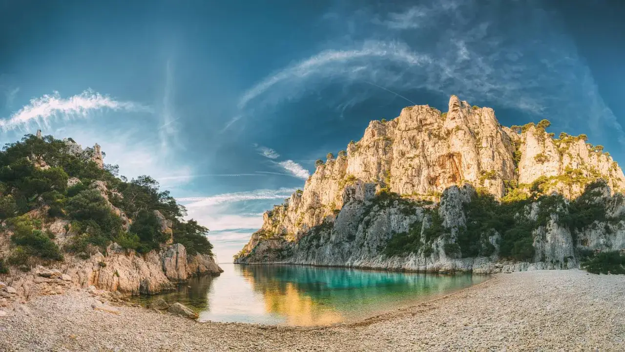 Malownicza zatoka z turkusową wodą i kamienistą plażą, otoczona skalistymi klifami porośniętymi zielenią. Idealne miejsce na wypoczynek w kurorcie na Riwierze Francuskiej.