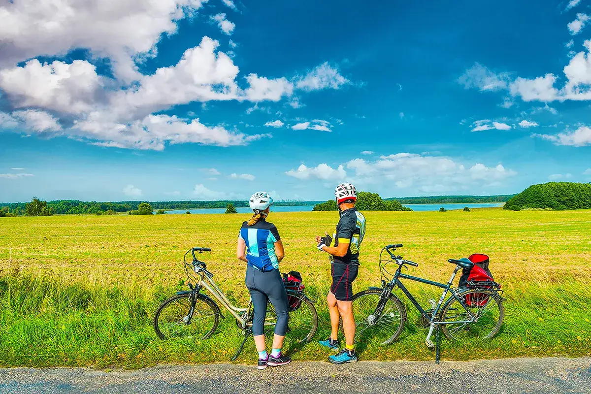 Para rowerzystów na malowniczej trasie koło Szczytna, odpoczywających na tle jeziora i pól.