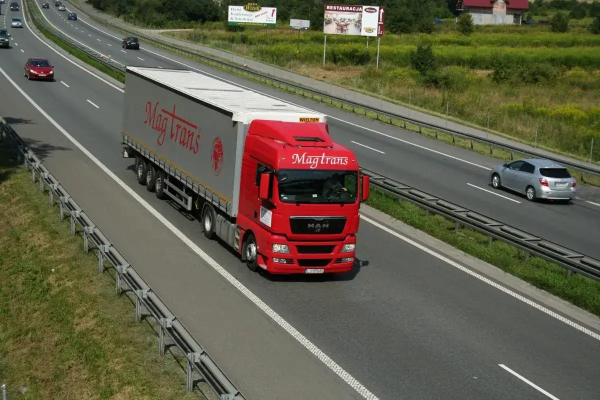 Czerwony tir z naczepą Magtrans jedzie autostradą. Kierowca może otrzymać mandat za wyprzedzanie tirem w niewłaściwym miejscu.