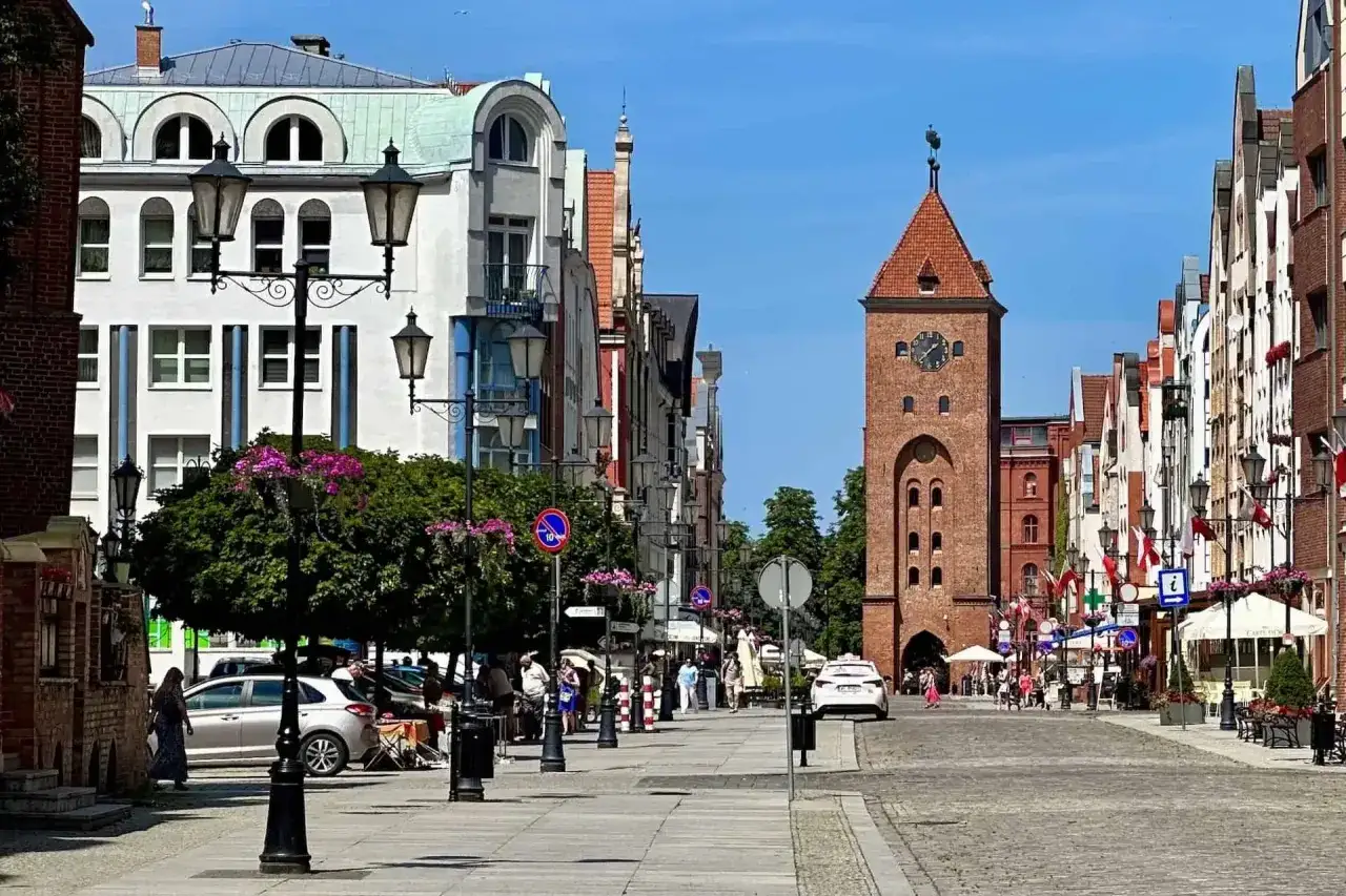 Ulica w starym mieście Elbląg z wieżą bramną i kolorowymi kamienicami.