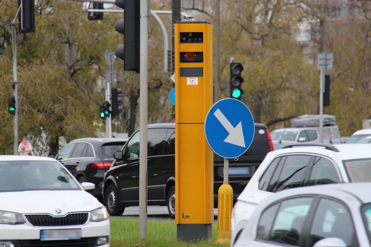 Żółty fotoradar przy drodze, obok znak kierunku jazdy. Czy przez fotoradar można stracić prawo jazdy? Uważaj na ograniczenia prędkości!