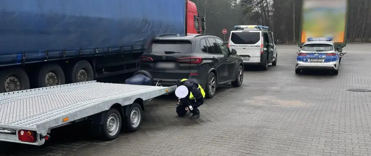 Kontrola drogowa: funkcjonariusz sprawdza, ile można jechać z przyczepką. Obok stoi czarny SUV, ciężarówka i radiowozy.