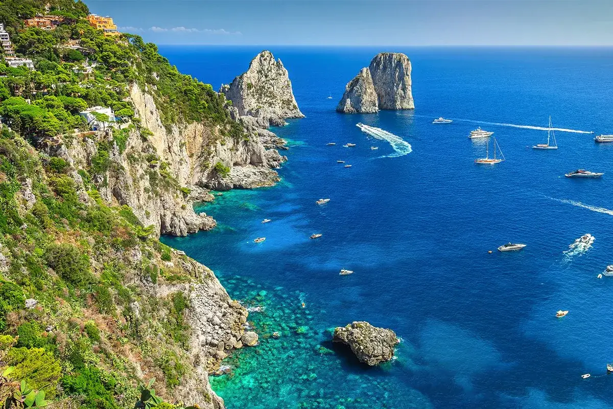Wyspa Capri: strome klify porośnięte zielenią, turkusowe morze i łodzie.