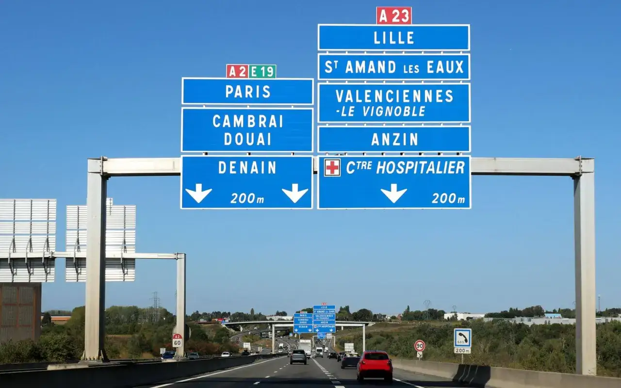 Znaki drogowe na autostradzie we Francji wskazują kierunki do Lille, Paryża, Valenciennes i centrum szpitalnego.