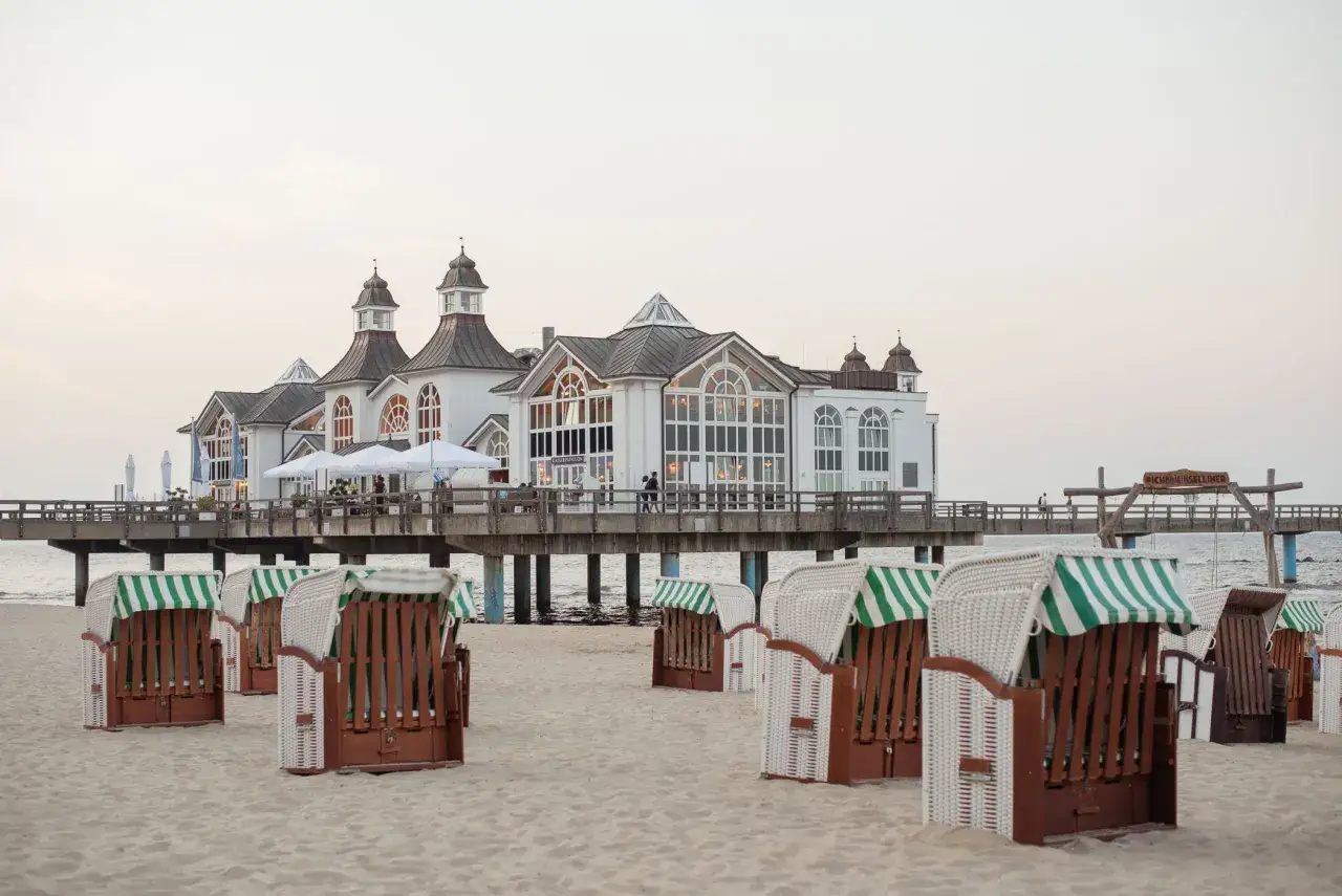 Plaża na wyspie Rugia z charakterystycznymi koszami plażowymi i molo z budynkiem Kaiserpavillon.