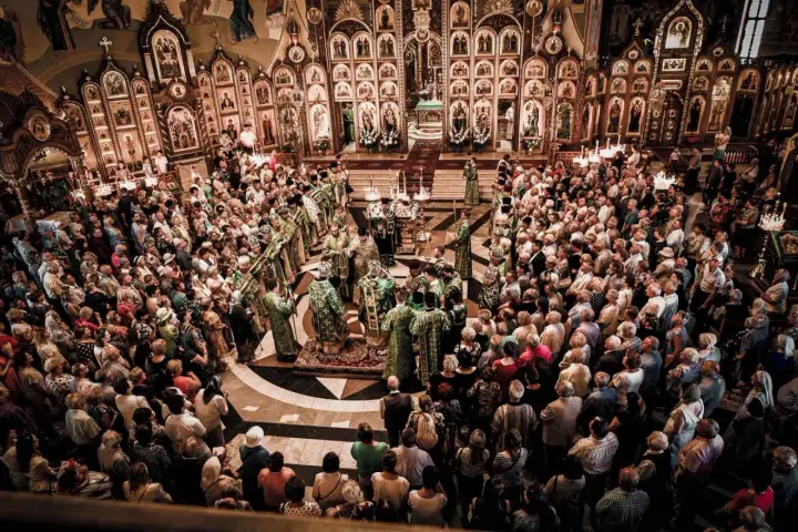Uroczysta liturgia w największej cerkwi w Polsce. Wierni zgromadzeni wokół ikonostasu, duchowieństwo w bogatych szatach.