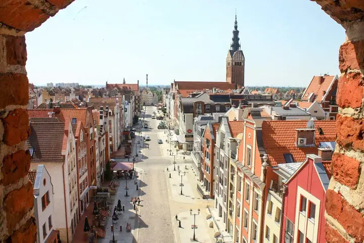 Widok na ulicę w **starym mieście Elbląg** z ceglanego muru. W oddali widać wieżę kościoła.