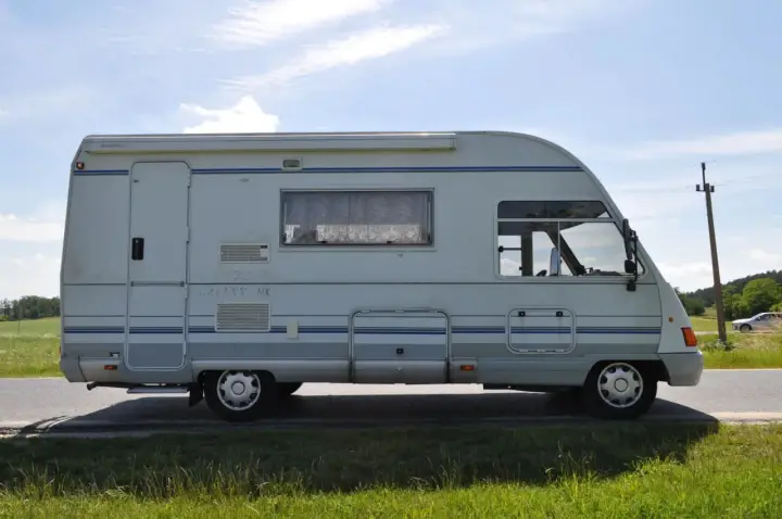 Biały ford galaxy camper z niebieskimi pasami stoi na poboczu drogi. W tle zielone pola i błękitne niebo.