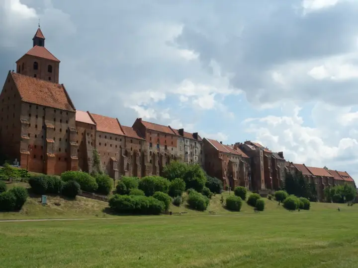 Zabytkowe miasto na trasie Ostróda-Grudziądz z ceglanymi budynkami i wieżą kościelną, otoczone zielenią i parkiem.